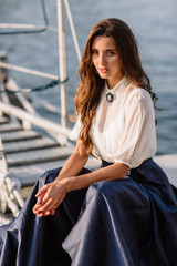 Beautiful girl walking on the pier by the sea near the yacht, boats in the blue long dress