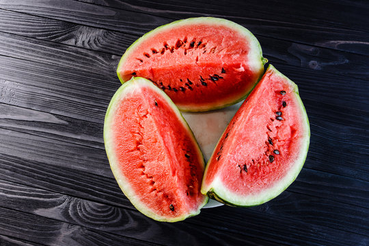 Background of three slices of a cut watermelon in a white plate on a black wooden table top view.