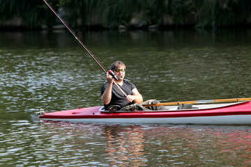 Junger Mann im roten Kajak beim Angeln im Fluss