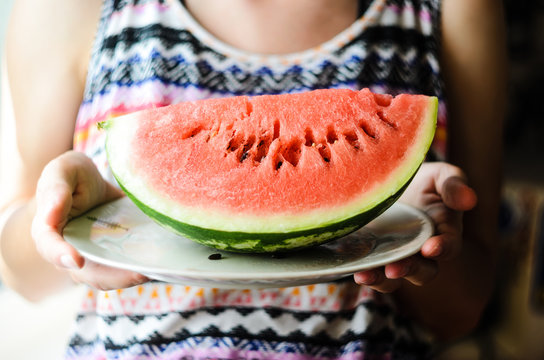 Watermelon background. Girl in a colorful summer shirt holding a plate with a large slice of watermelon in the sun