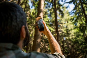 Active young adult man enjoy taking photograph in wild pine forest on mountain in sunny summer day outdoor