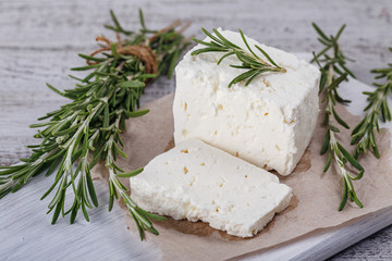 Fresh feta cheese with rosemary on white wooden serving board