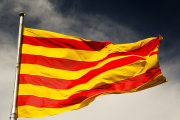 A close-up shot of a large sunlit Catalan flag against a dark sky