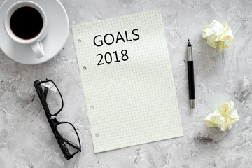 Goals list for 2018. Sheet of paper near pen, glasses and cup of coffee on grey stone background top view mockup