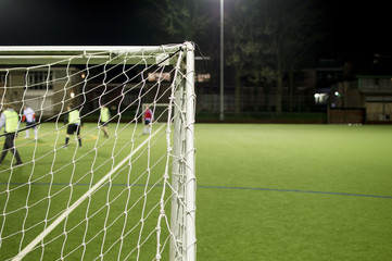 Fototapeta premium Behind Football Goalposts During Amateur Game On Floodlit Pitch