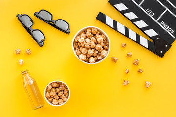 Snacks for film watching. Popcorn and soda near clapperboard, glasses on yellow background top view copyspace