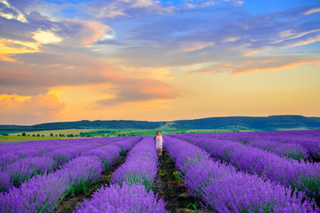 Fototapeta na wymiar Happy girl in platitse rejoices and runs in the lavender field at sunset