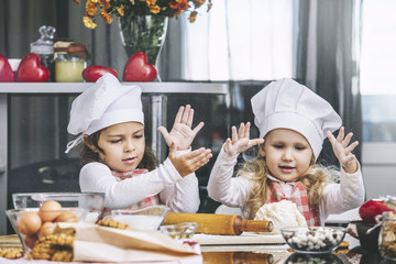Two happy little girls child cook with flour and dough at the table in the kitchen is lovely and...