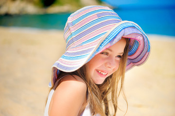happy girl in a beach hat sits on sand near the sea, plays and laughs © Tortuga