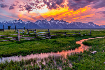 Golden Fiery Sunset at Grand Teton - A colorful spring sunset at Teton Range, seen from an abandoned old ranch in Mormon Row historic district, in Grand Teton National Park, Wyoming, USA.  - obrazy, fototapety, plakaty