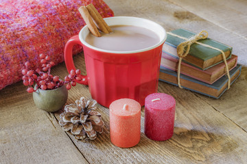 Red mug of hot chocolate with cinnamon sticks in it on rustic wood table, autumn