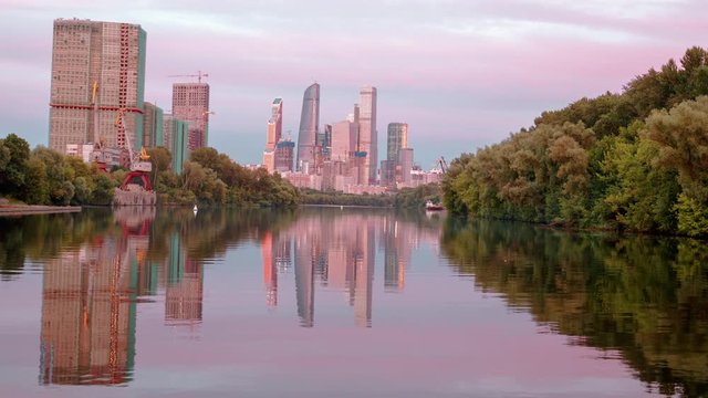 Hyperlapse view on the Moscow City from the boat. Moscow International Business Centre and it's reflection in the river at sunset time. Industrial port cranes and construction site on foreground.