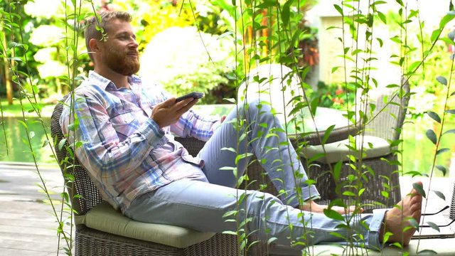 Handsome man chatting on loudspeaker while relaxing in the garden
