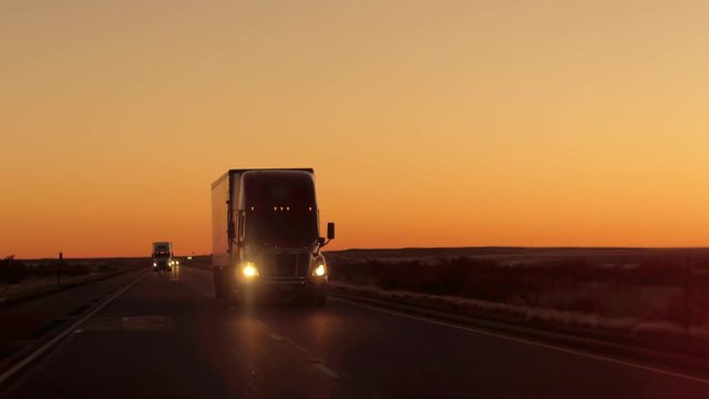 CLOSE UP LENS FLARE: Semi truck driving and hauling goods on empty highway across the Great Plains in golden morning. Freight delivery truck transporting cargo on interstate freeway at stunning sunset