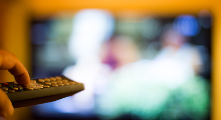 ein Mann schaltet mit einer Fernbedienung einen Fernsehapparat an