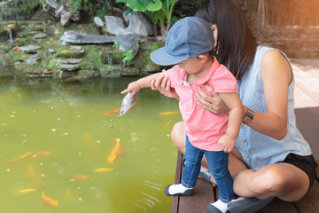 Asian beautiful mother is take care your cute baby feeding fish in garden.