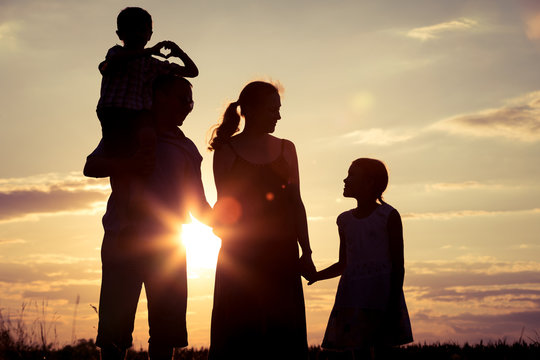 Happy family standing on the field at the sunset time.