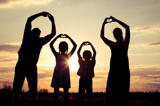 Happy family standing on the field at the sunset time.