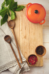 Black and red pepper, basil leaves,  ceramic pan,  wooden stand, simple old spoons and  linen napkin on light background. Kitchen accessories concept. Selective focus. Top view. Toned image.