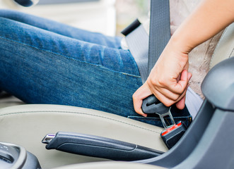 Fototapeta premium Closeup woman hand sitting inside car fastening seat belt. Safety belt safety first.