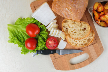 Breakfast from bread, cheese, tomatoes, potatoes and all-over salad on a wooden table closeup.
