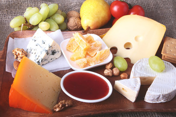 Assortment of cheese with fruits, grapes and nuts on a wooden serving tray.