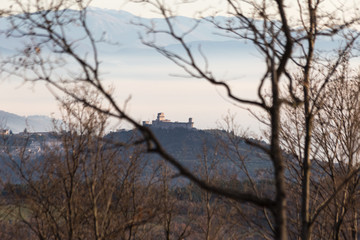 A view of Rocca Maggiore (Assisi, Umbria) through some out of focus trees, over a sea of fog filling the valley