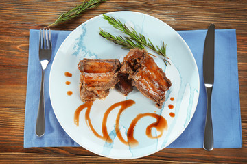 Plate with delicious ribs on wooden table