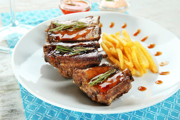 Plate with delicious ribs and french fries on table