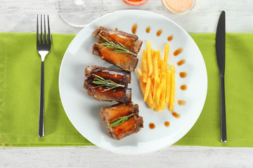 Plate with delicious ribs and french fries on table