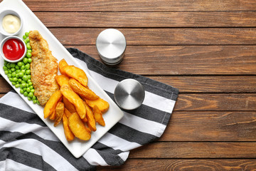Plate with fried fish and chips on wooden background