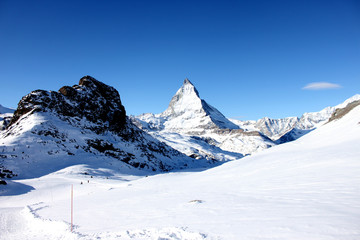 Scenic view on snowy Matterhorn peak in sunny day with blue sky and some clouds in background