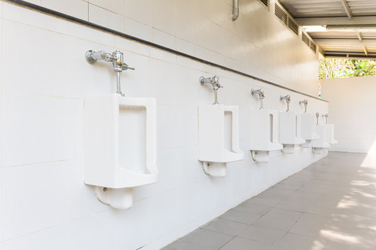 Row of white urinal for men on tile wall in toilet.