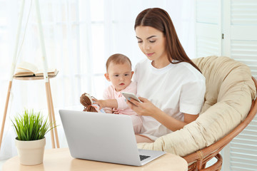 Young mother holding baby while working in home office