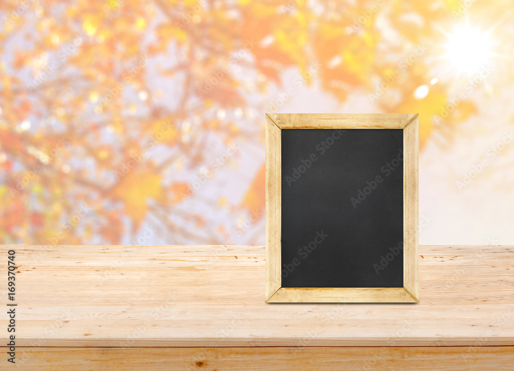 Poster blackboard on wood table top with blur maple leaf with sunlight background,autumn backdrop,mock up f