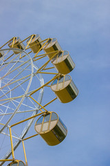 Ferris wheel with yellow round cabs against the blue sky in summer