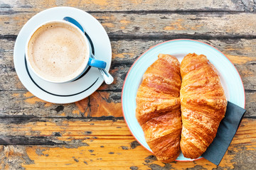Cup of coffee with milk and croissants, on wooden table