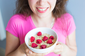 Woman's hands hold healthy and natural breakfast, oatmeal and raspberries in a bowl