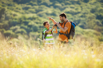 Father and son are hiking in nature in summer. They are using binoculars. 