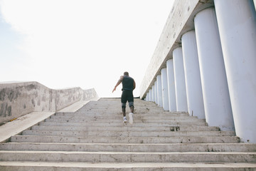Rear view of a male athlete running up staircase outside building
