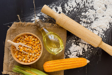 Corn kernels and Corn oil in bottle on black wooden background