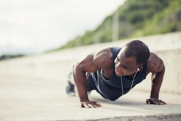 Portrait of a young black man doing push ups at the beach - Powered by Adobe