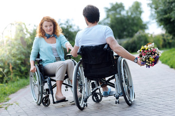 Pleasant wheelchaired man presenting flowers her wife