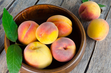 Wooden bowl with peaches on wooden background