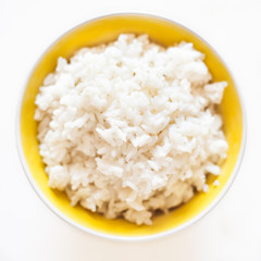 White cooked  rice in a  yellow  bowl over white background close up.