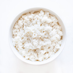 White cooked  rice in a white bowl over white background close up.