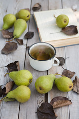 Hot tea, book, pear and autumn leaves on wood background.autumn relaxation concept