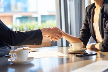 Close-up shot of unrecognizable business partners shaking hands while having negotiations at...