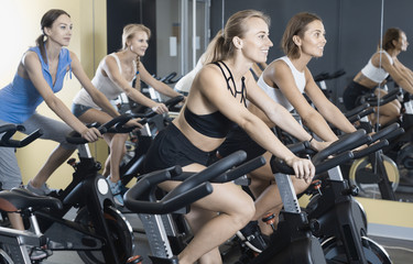 Fototapeta na wymiar Girls during workout on stationary bicycle in fitness gym