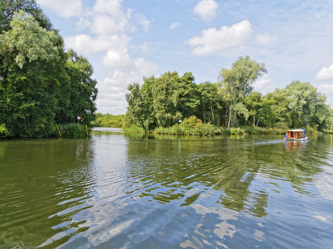 A small cabin cruiser sailing on the River Bure, near Wroxham on the Norfolk Broads, passes the entrance to Bridge Broad.